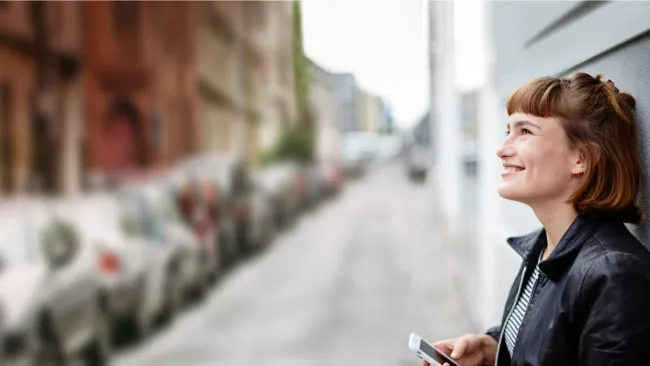 Woman with phone leaning against building