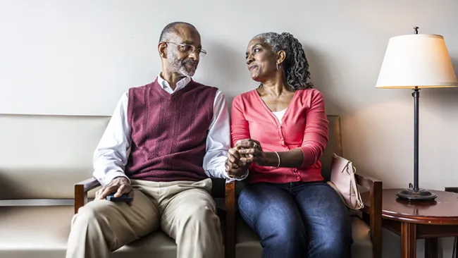 An elderly couple sitting and holding hands in a doctor's office waiting room 