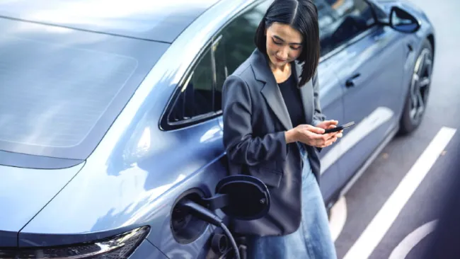 Woman leaning against her car while it charges