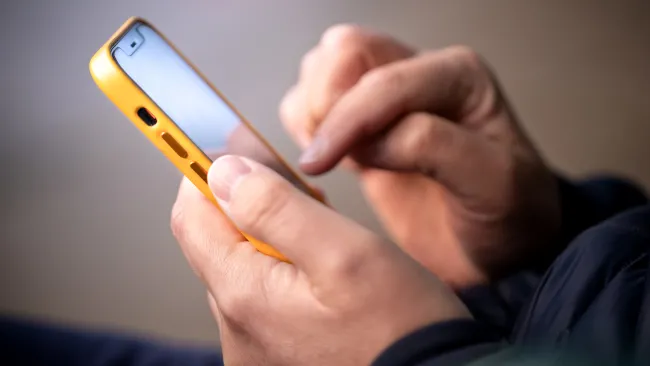 A person's hands checking a smartphone with a yellow cover