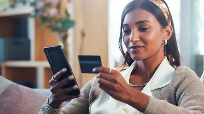 Woman sitting on her couch and entering her credit card information into her phone