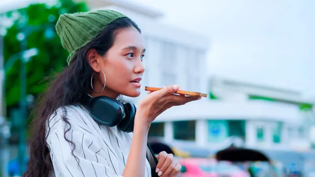 Woman wearing headphones around her neck and talking into a smartphone