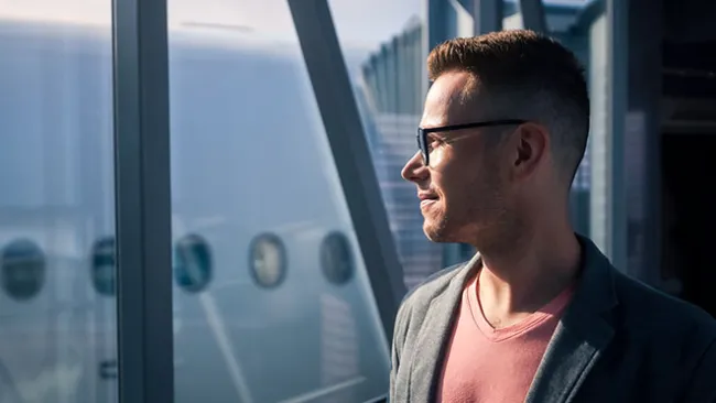 Smiling man looking out the window of an airport 