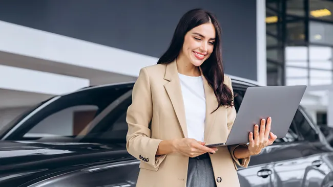 A woman standing outside her vehicle and holding a laptop 