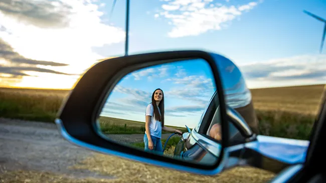 Woman standing next to a car, shown in a car's side mirror