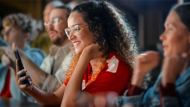 A woman with a curly hair and glasses smiling while looking at her phone