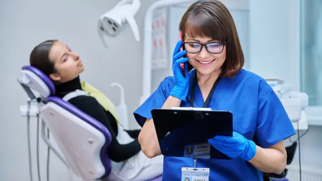 Dentist on the phone with a patient in the chair behind
