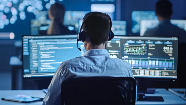 Man wearing a headset looking at a computer screen full of data 