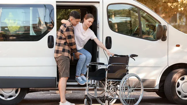 A man assisting a seemingly disabled woman step out of a white van