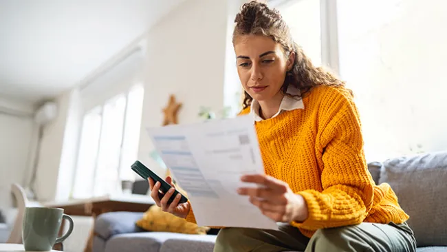 Woman looking at a bill and holding a phone