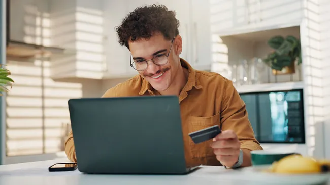 A man working on a laptop while holding a debit or credit card