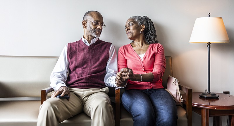 An elderly couple sitting and holding hands in a doctor's office waiting room 