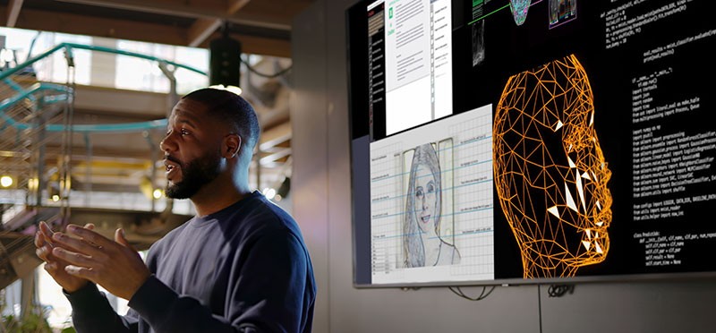 Man standing in front of computer screens that show digital/futuristic images of people