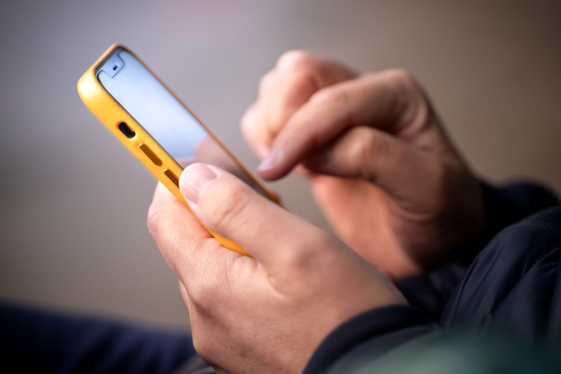 A person's hands checking a smartphone with a yellow cover