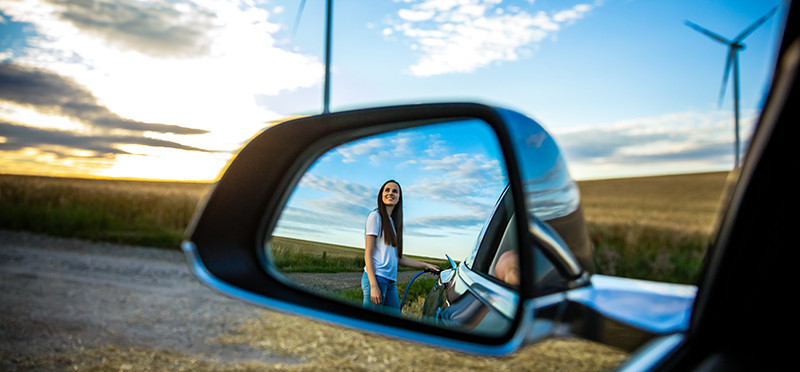 Woman standing next to a car, shown in a car's side mirror