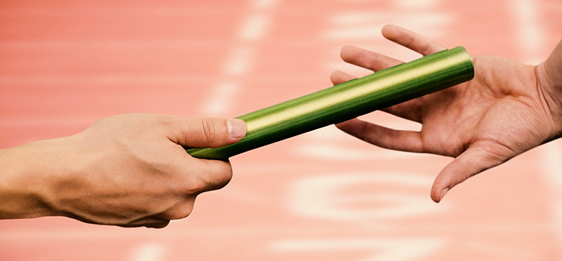 One person's hand handing a relay baton to another hand