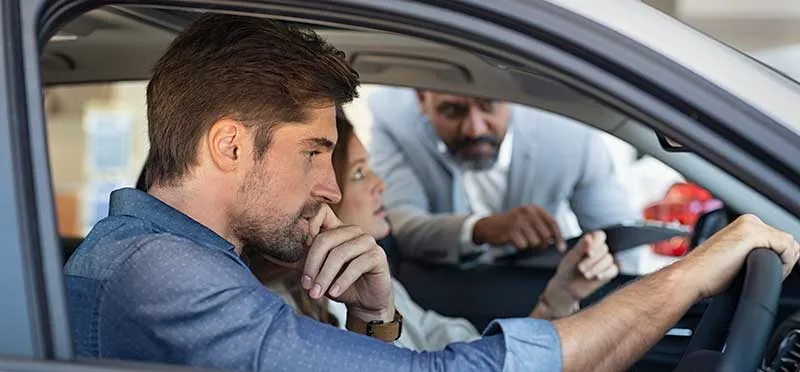 Man and woman sitting in a can speaking to a man who's leaning in the front window.