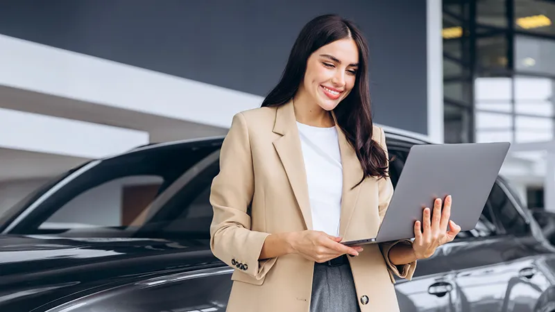 A woman standing outside her vehicle and holding a laptop 