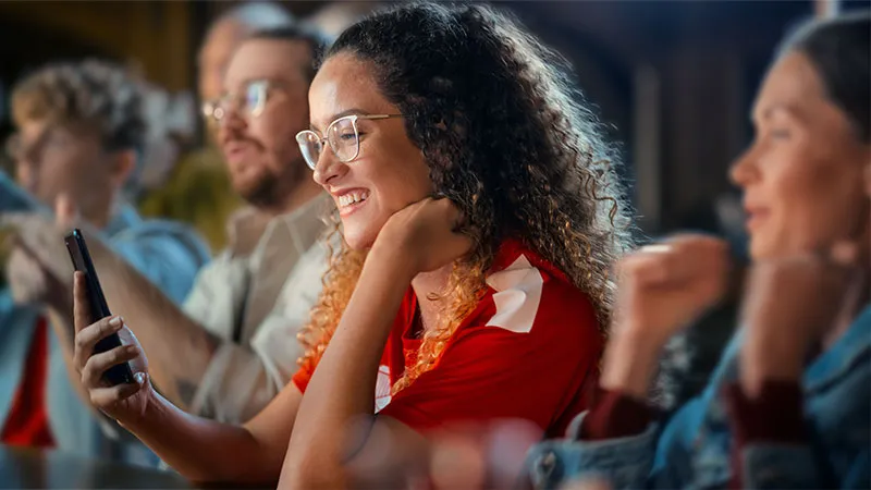 A woman with a curly hair and glasses smiling while looking at her phone