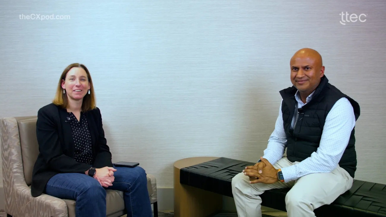 Two people sitting and smiling at a camera. Business setting. 