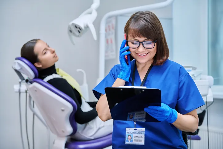 Dentist on the phone with a patient in the chair behind