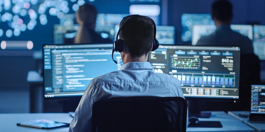 Man wearing a headset looking at a computer screen full of data 