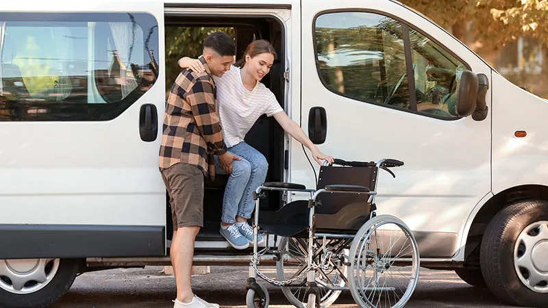 A man assisting a seemingly disabled woman step out of a white van