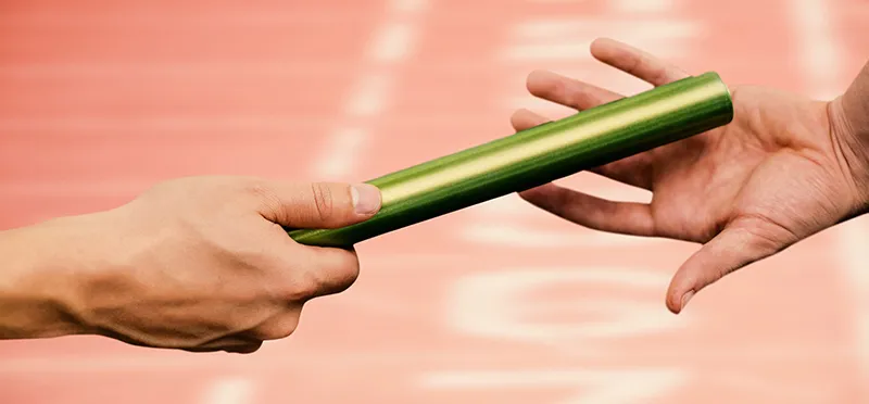 One person's hand handing a relay baton to another hand