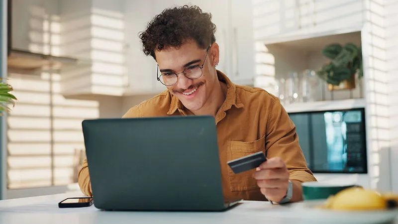 A man working on a laptop while holding a debit or credit card